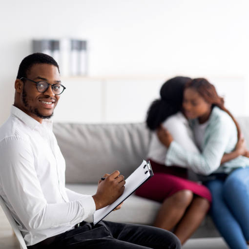 male psychologist smiling with two women hugging in the background